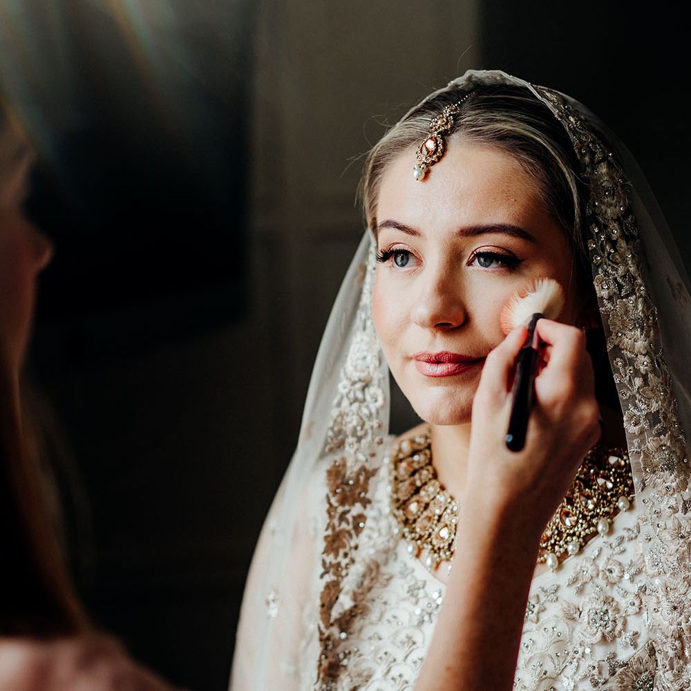 Blonde bride has her makeup done the morning of her wedding day with light pink lipstick and winged eyeliner for a natural look