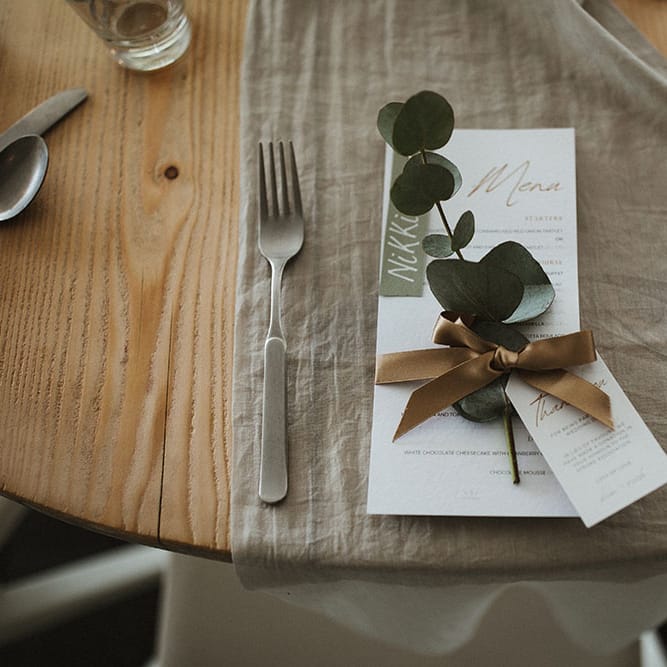 Sage green fabric table runner on wooden table with white stationery tied with brass coloured silk ribbon