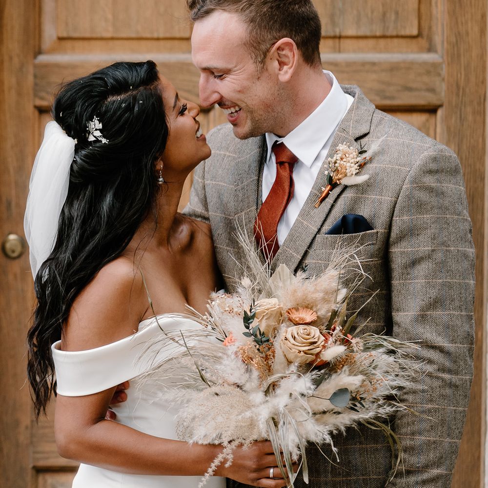 Bride and groom laugh together on the day of their outdoor wedding at The Great Tythe Barn venue 