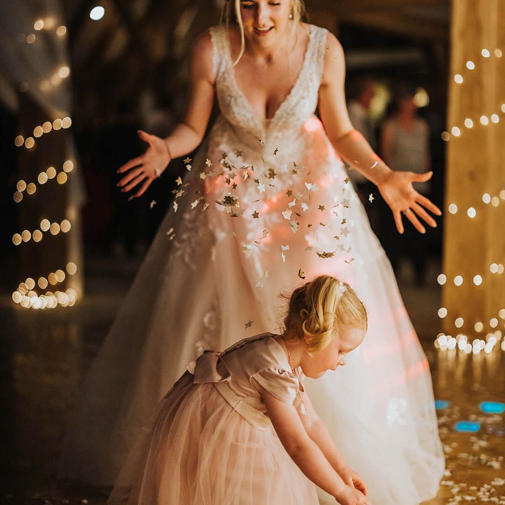 Bride in a lace beaded wedding dress throws confetti over a little girl in a pink tulle dress