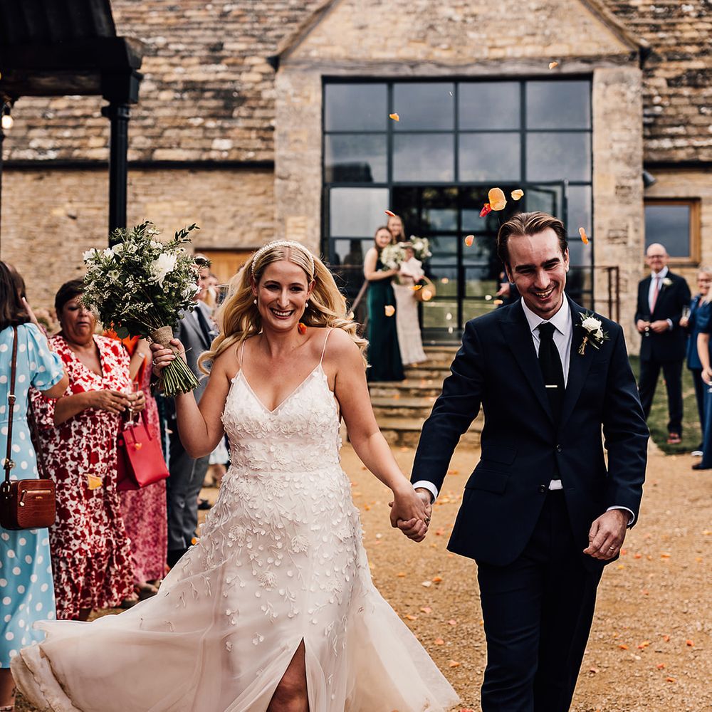 Bride in an Alexandra Grecco Lana wedding dress and groom in a dark blue suit have their confetti moment after the ceremony 