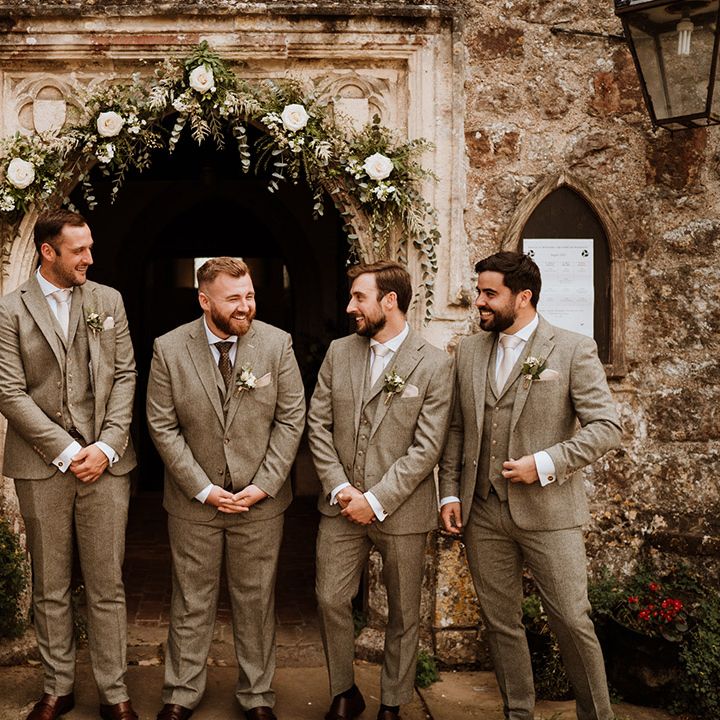 Groom and groomsmen laughing together in three piece grey suits with white flower buttonholes 