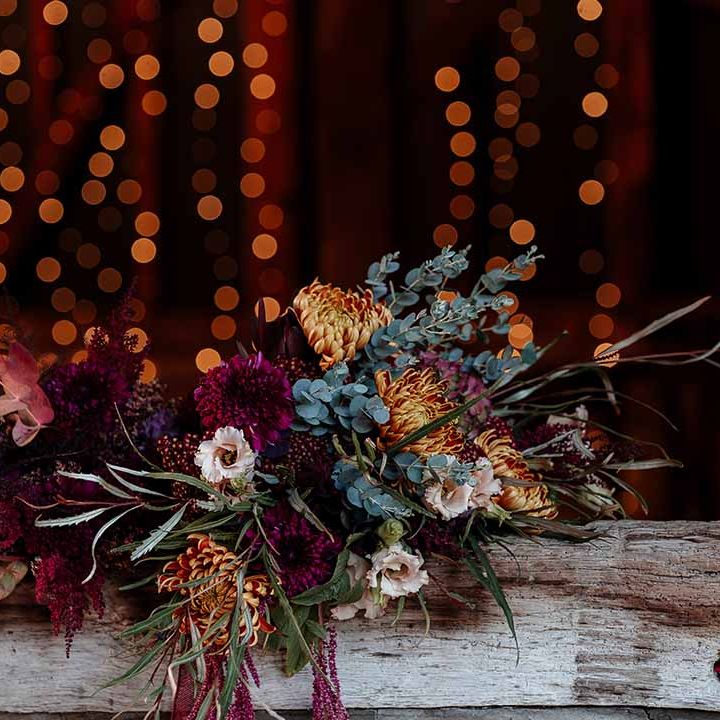 Autumnal dried flower wedding bouquet with peonies, roses and foliage with fairy lights in the background 