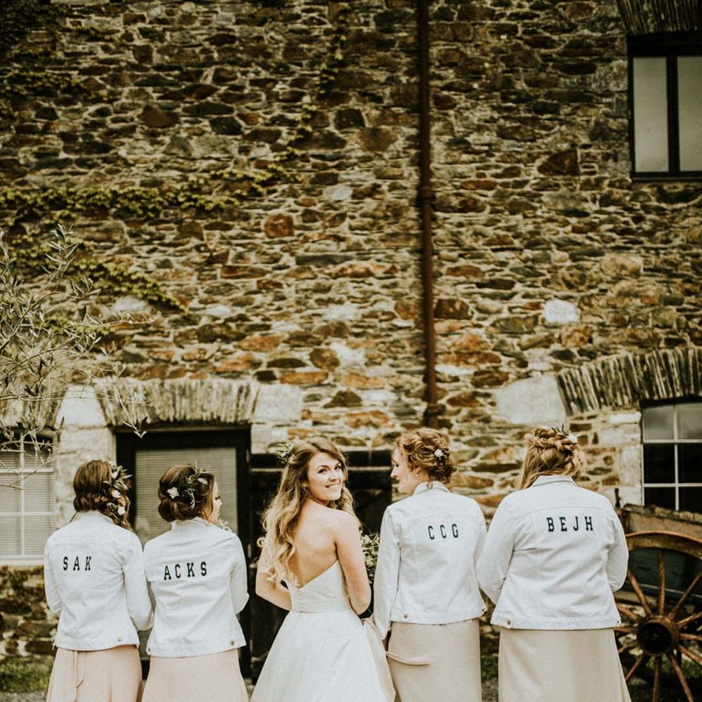 Bridesmaids in white denim jackets with their nicknames on the back with the bride for fun bridal party wedding photo 