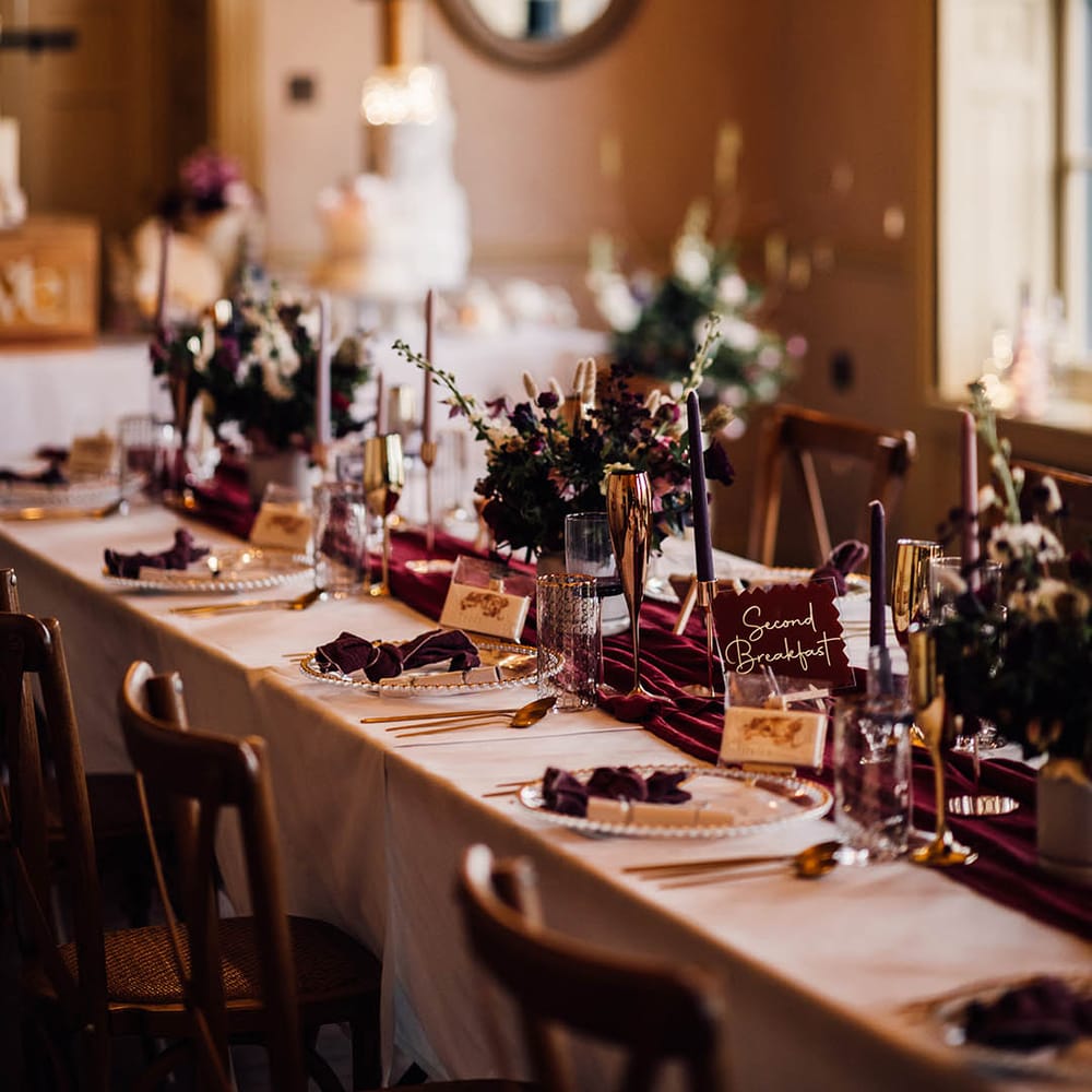 Burgundy wedding tablescape for winter wedding with beaded charger plates, gold rimmed glasses and table name signs 