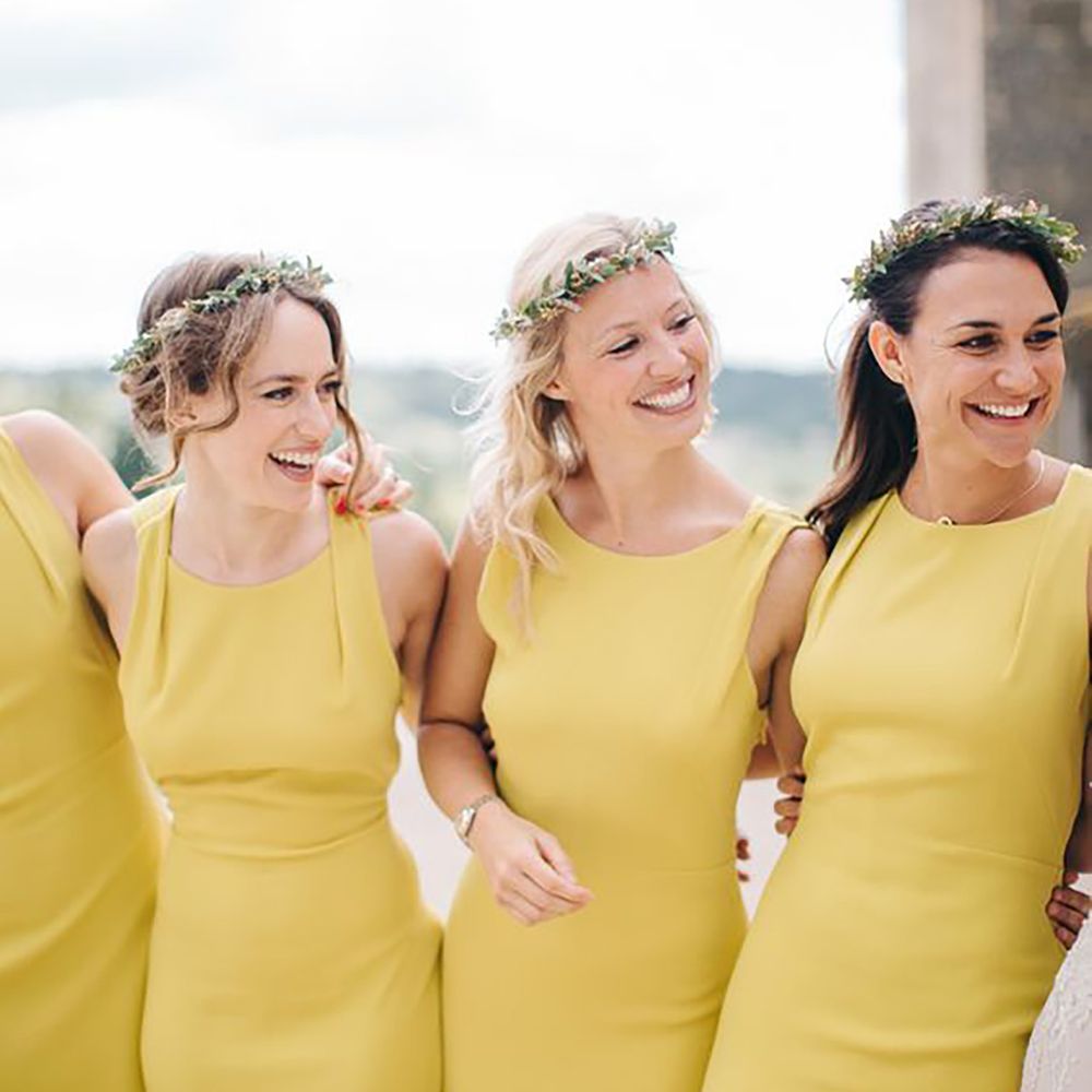 Four bridesmaids standing arm in arm smiling wearing yellow bridesmaid dresses by M&J Photography
