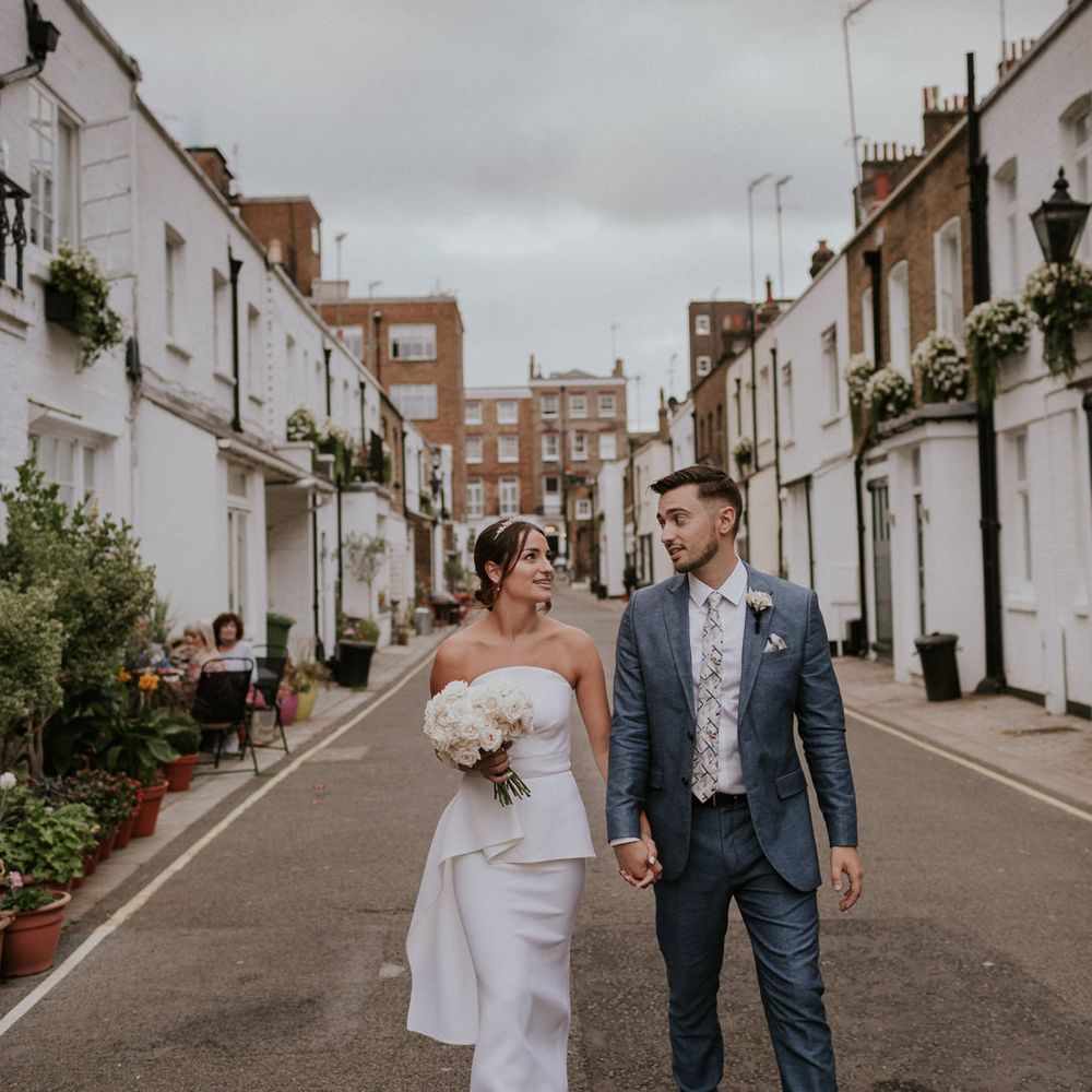 Bride in layered Roland Mouret dress with white bouquet holding hands with her husband