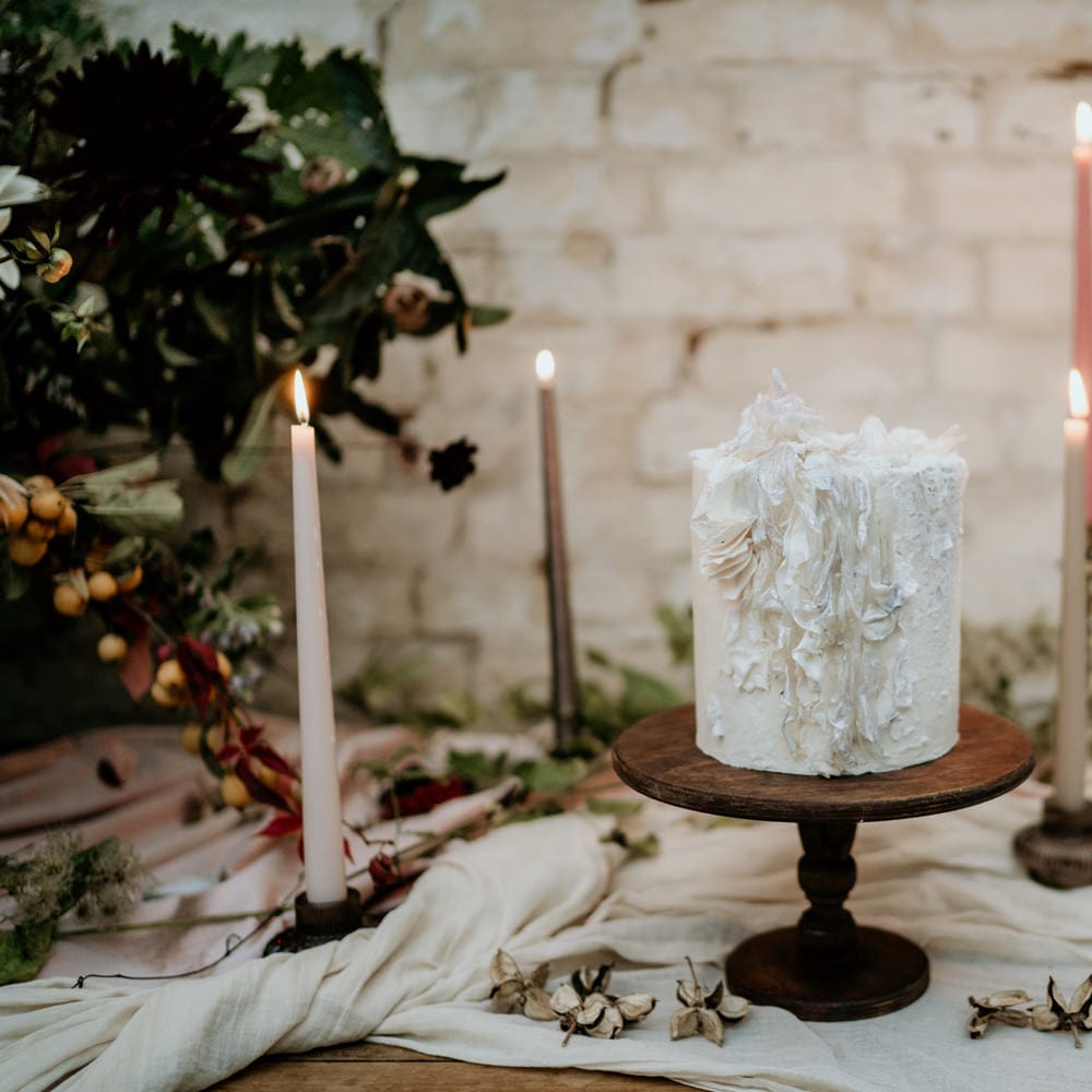 Single tier wedding cake for elopement wedding resting on a wooden cake stand surrounded by coloured taper candles 