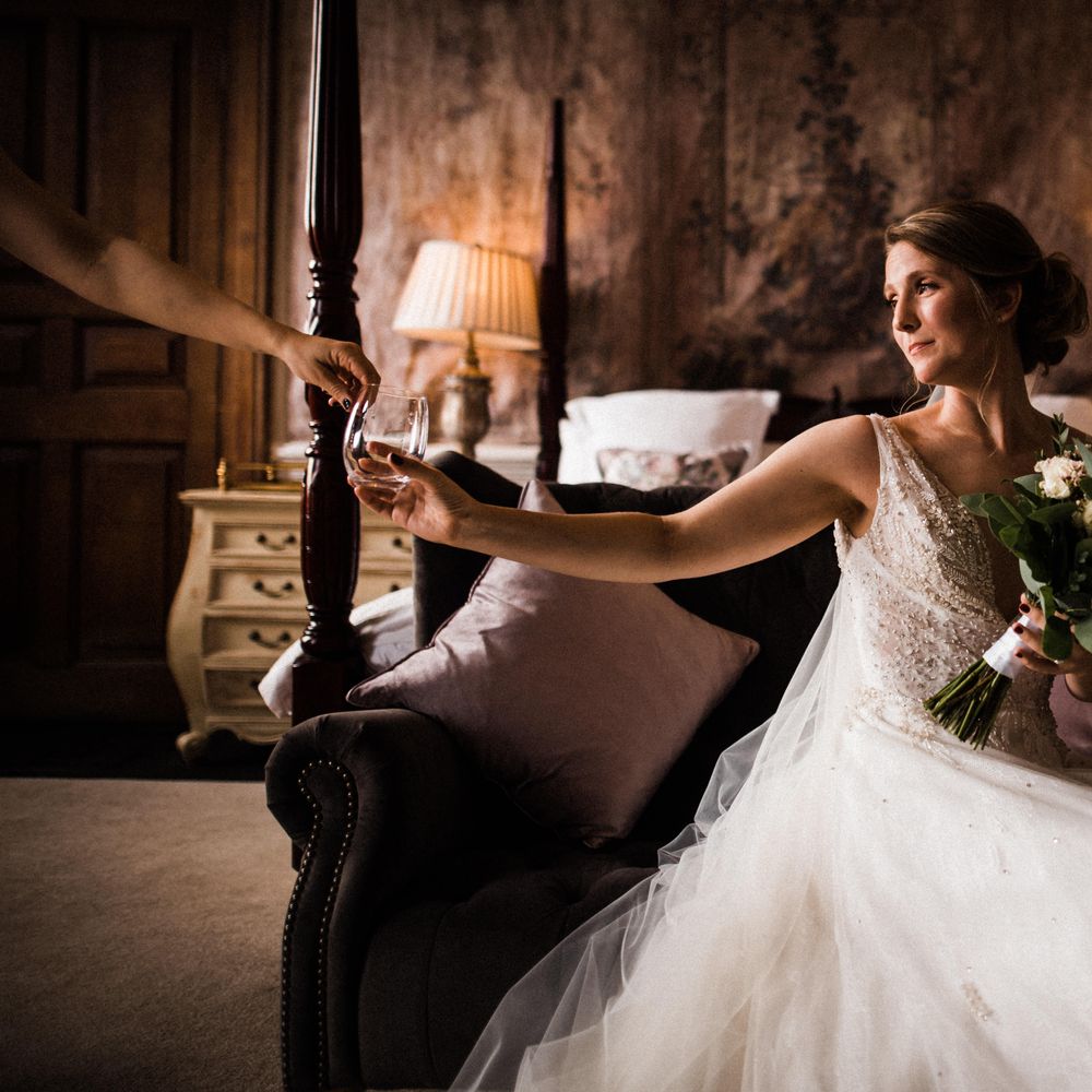 Bride sits in front of four poster bed holding white floral bouquet