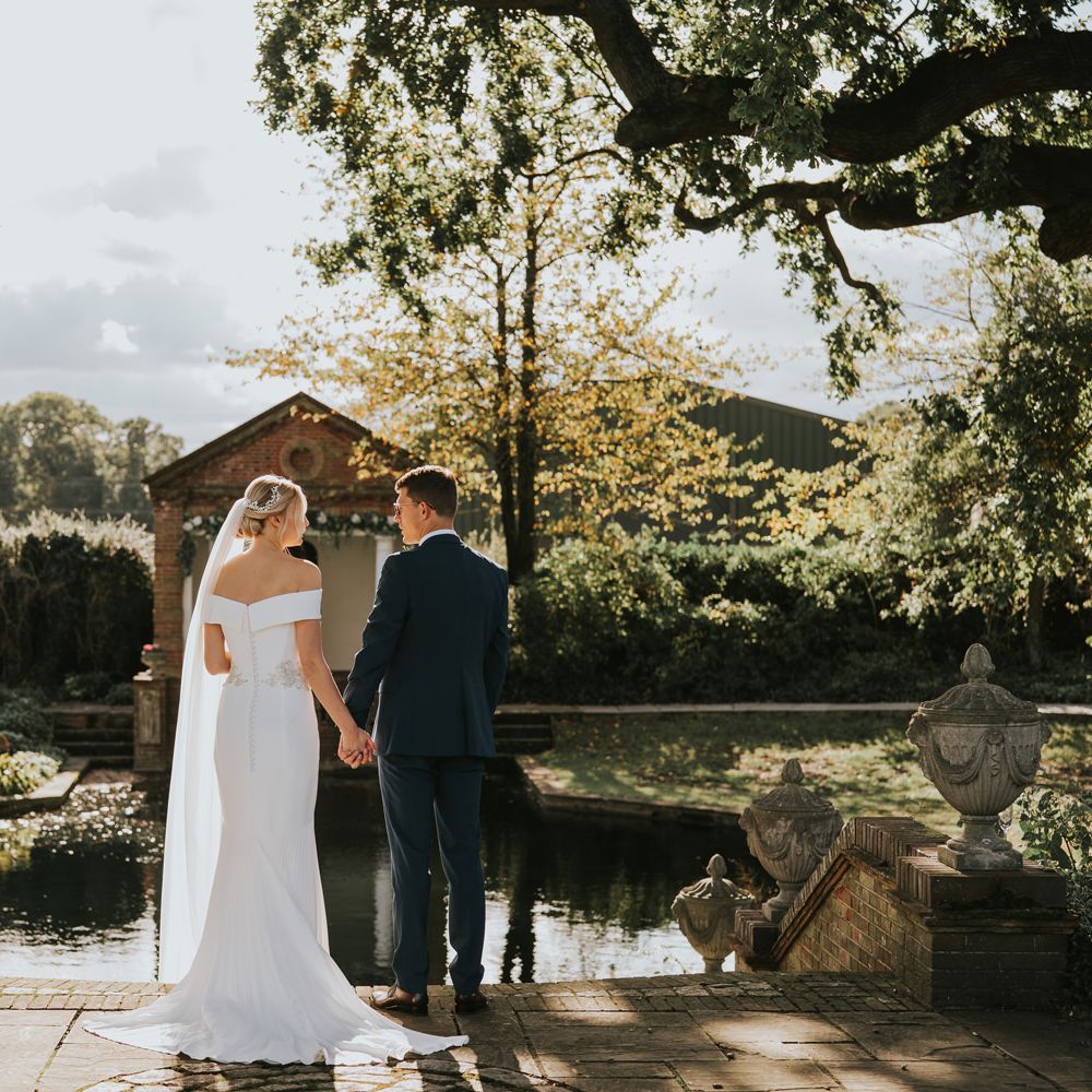 Bride & groom hold hands beside pond in the sunshine