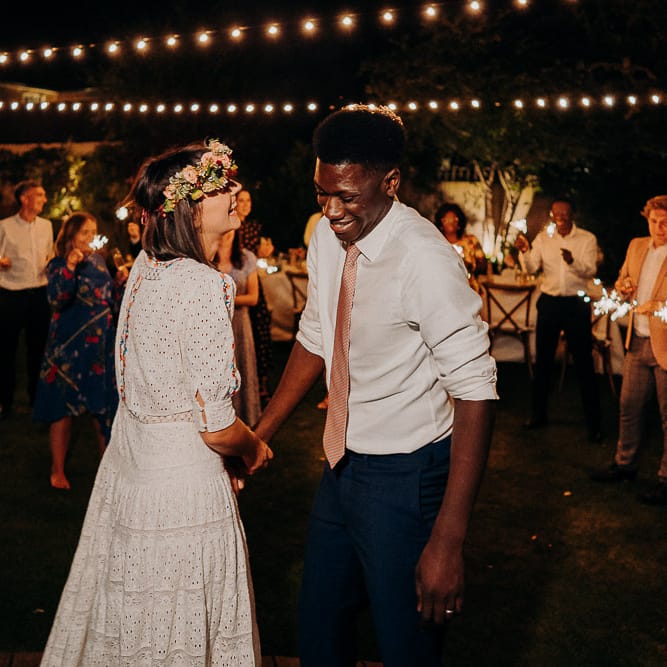 outdoor wedding first dance under a canopy of festoon lights and surrounded by guests waving sparklers