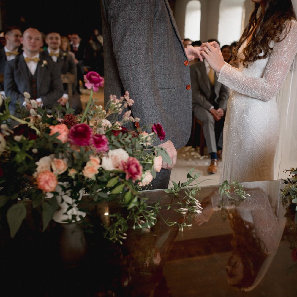 Bride and groom exchanging rings, with vibrant pink flowers - bride wears beaded long sleeve bridal gown 