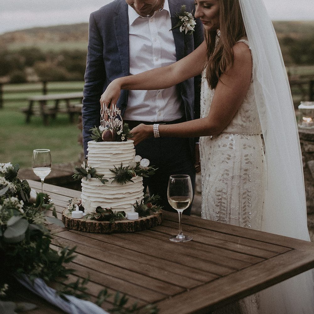 Bride & groom cut cake outdoors on the day of their wedding