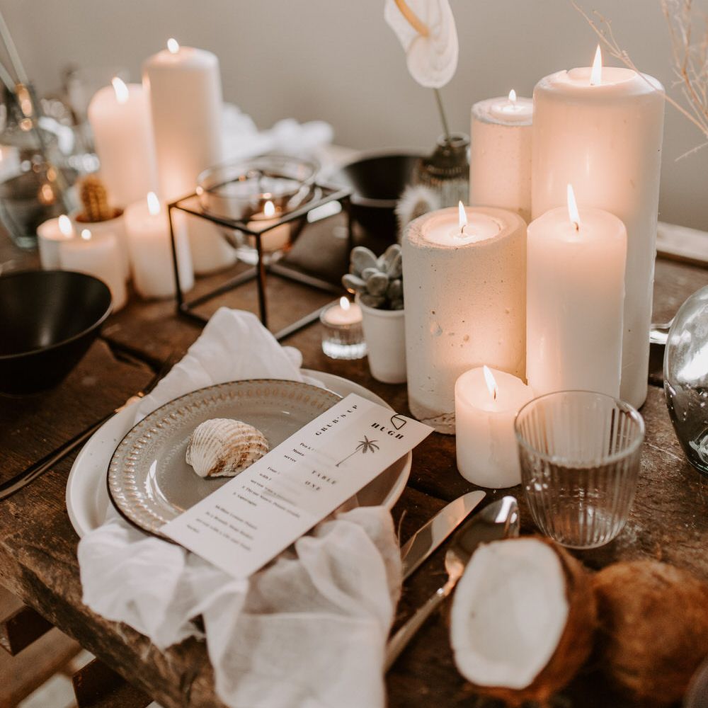 White pillar candles and tropical black and white neutral tablescape details including shells and coconut husks