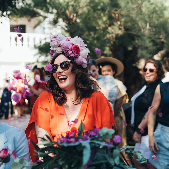 Bride walks through guests on her wedding day wearing her dark hair in curls and pink floral crown