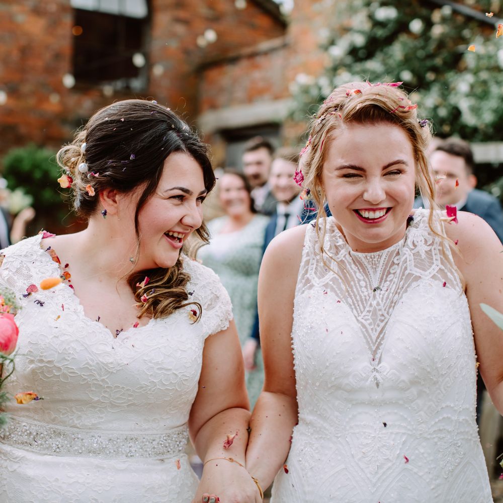 Brides laugh and walk through confetti together on their wedding day