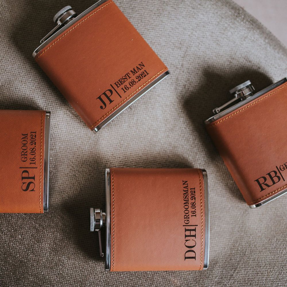 Four orange leather hip flasks with personalised initials on chair at Tythe Barn wedding with barn wedding flowers