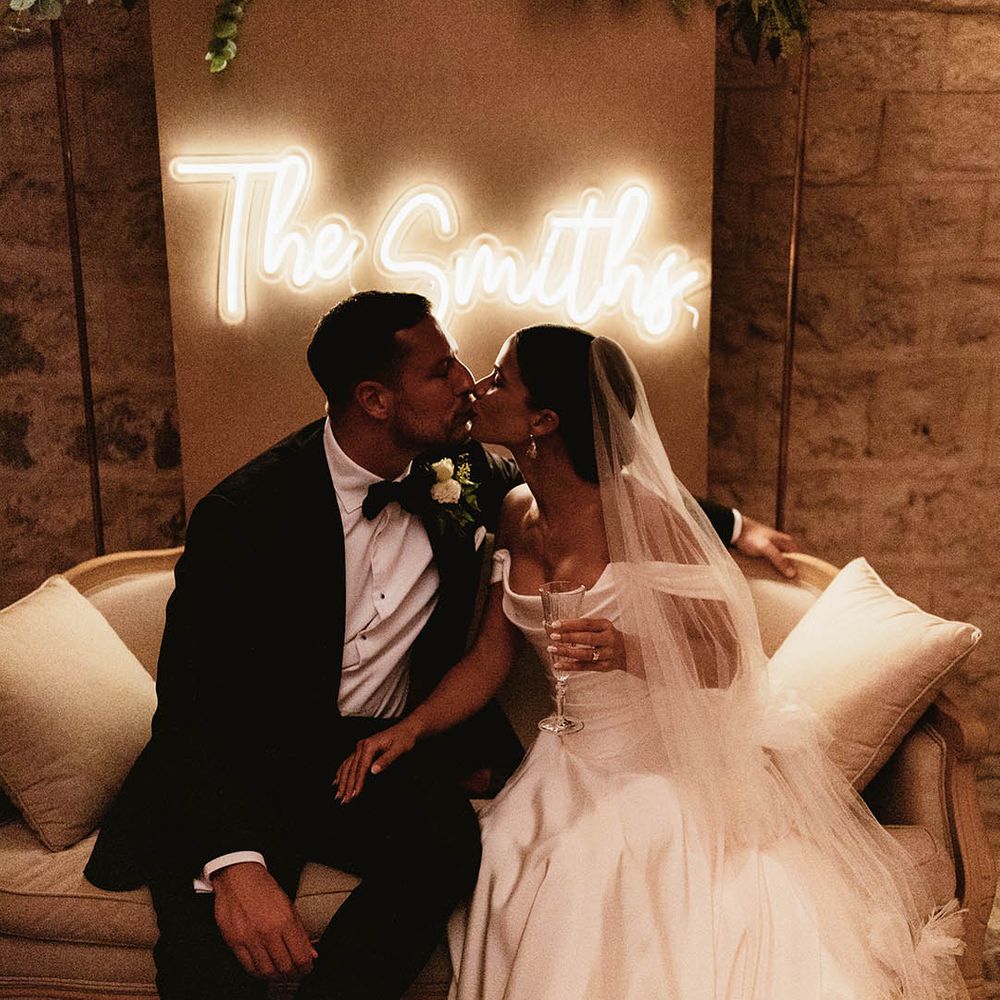 Bride & groom sit in front of personalised neon sign