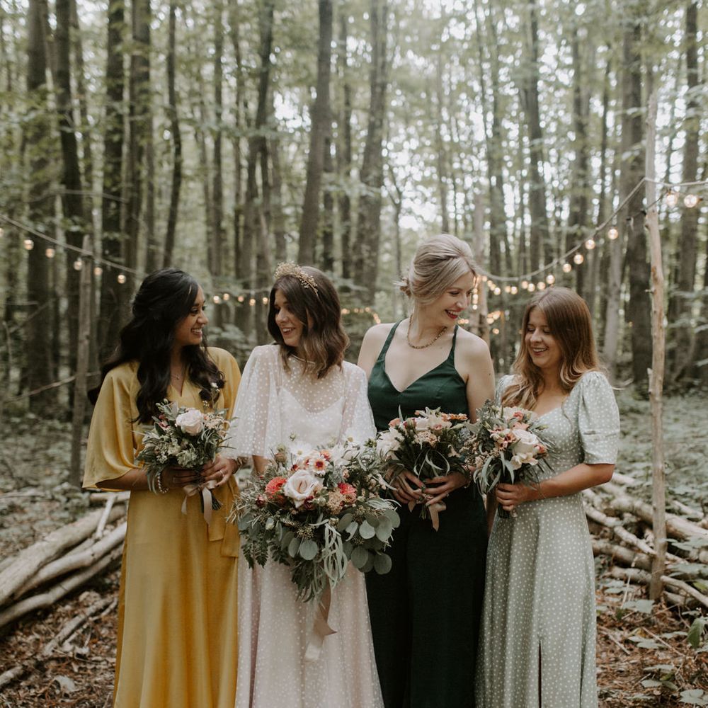 Bride stands with her wedding party who all wear different style and coloured gowns whilst holding floral bouquets