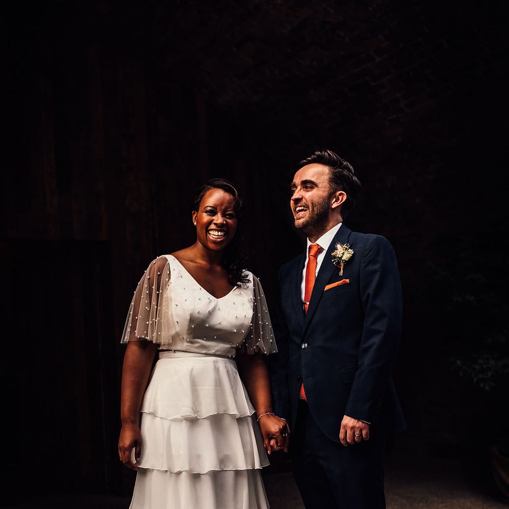 Groom in a navy suit with orange tie holding hands with his Black bride in bridal separates 