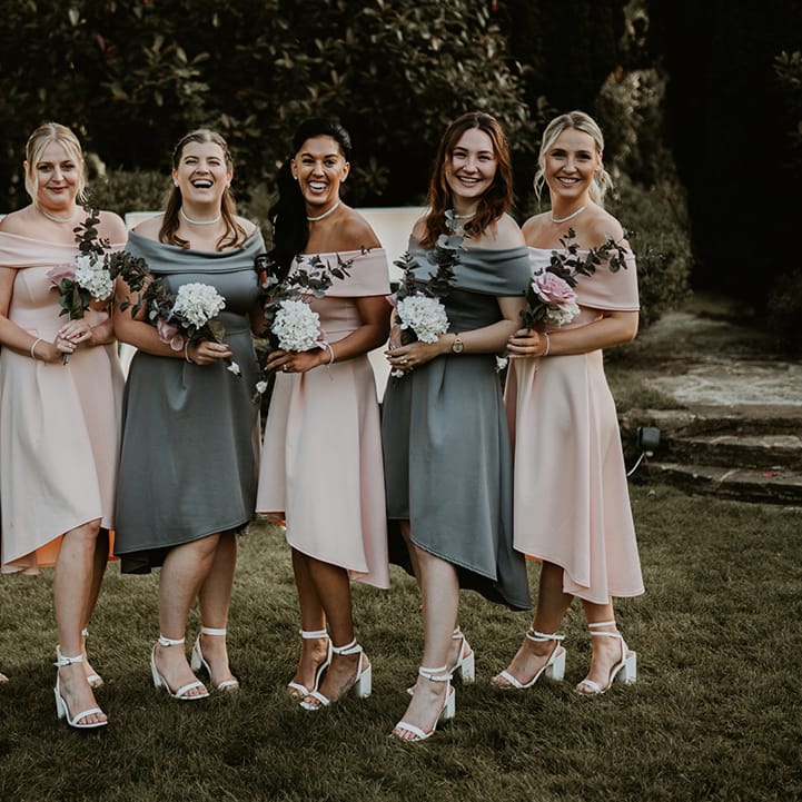 Bridesmaids wear tea length gowns complete in pastel pink and sage green