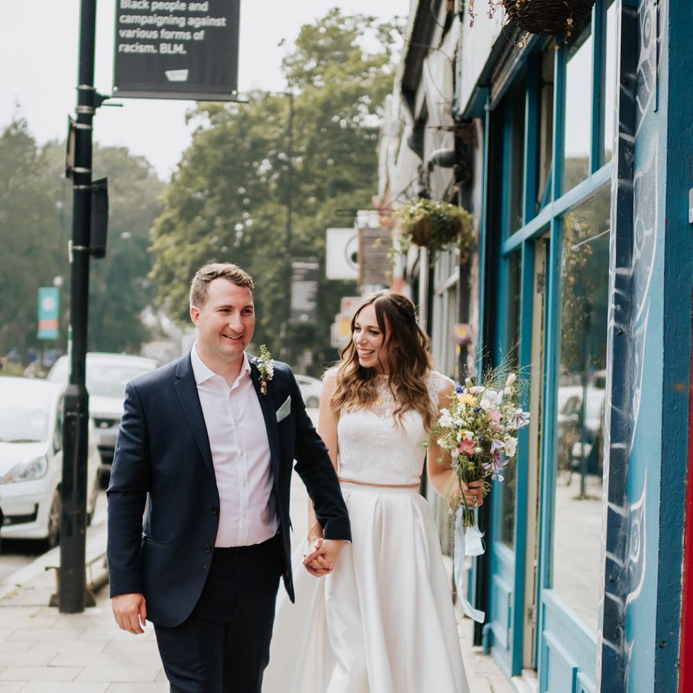 Bride and groom walking the streets with bride in high low pleated wedding skirt and electric blue wedding shoes 