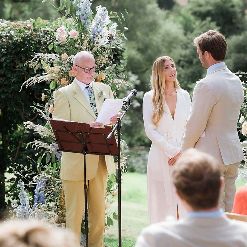 Bride at groom at their outdoor summer wedding with pastel flower displays and bespoke ceremony