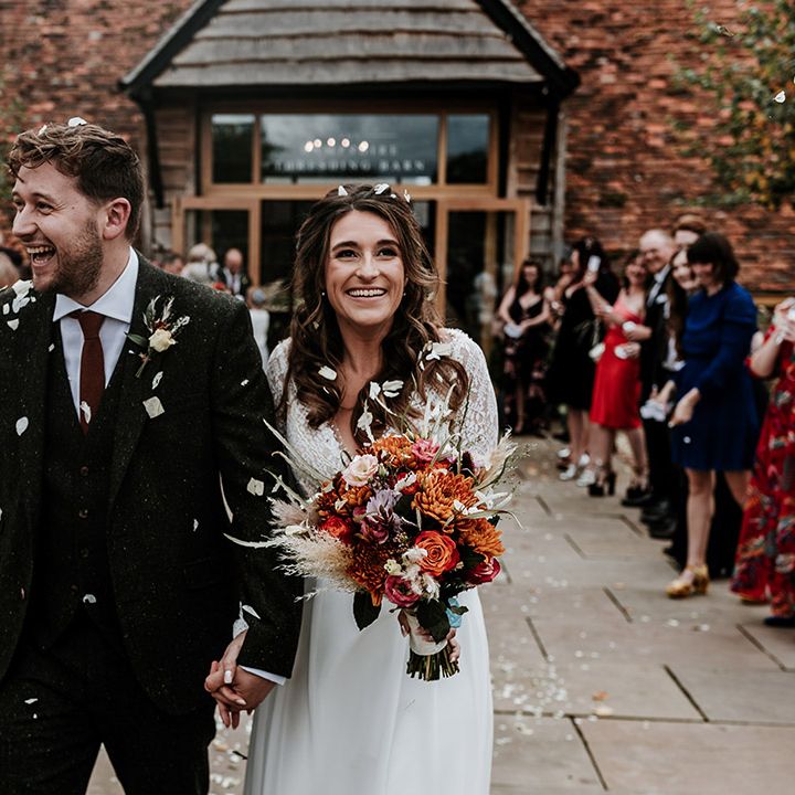 Bride and groom have confetti exit with bride holding bright orange autumnal wedding bouquet 