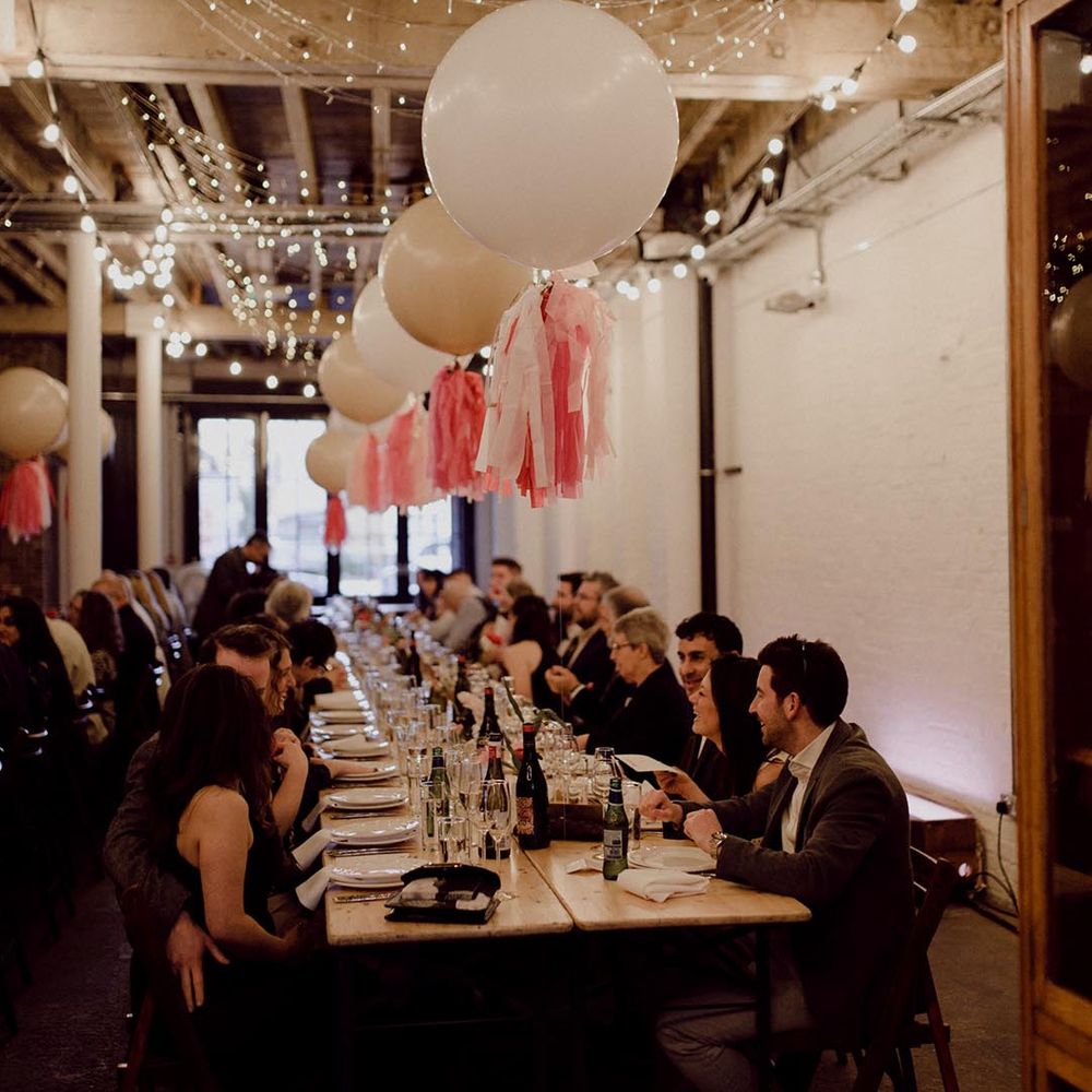Large white balloons with pink tissue paper tassels and fairy lights decorate the wedding reception at industrial wedding venue 