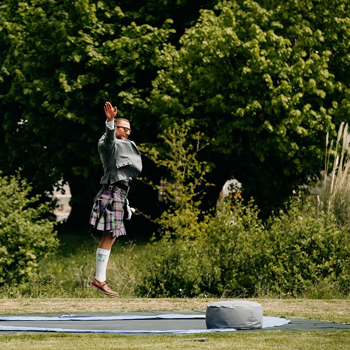 Wedding guest wearing a kilt has fun on a trampoline 