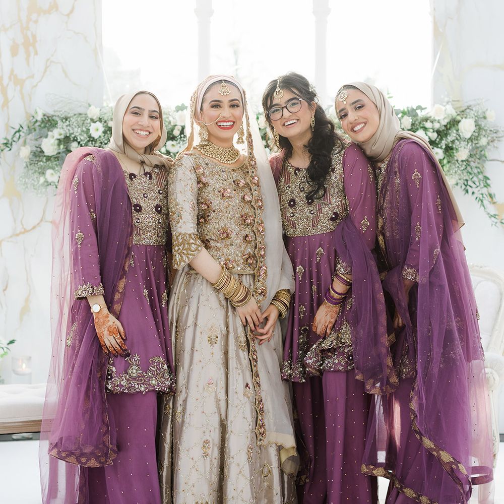 Bride stands with her bridesmaids who wear purple saree's complete with gold embellishment 