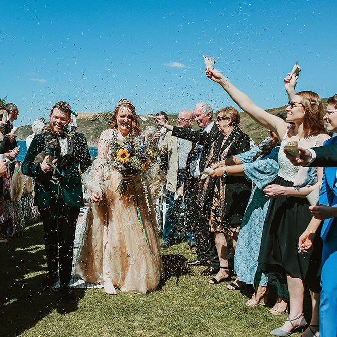 Bride & groom walk through confetti after outdoor wedding ceremony on the beach front in Cornwall 