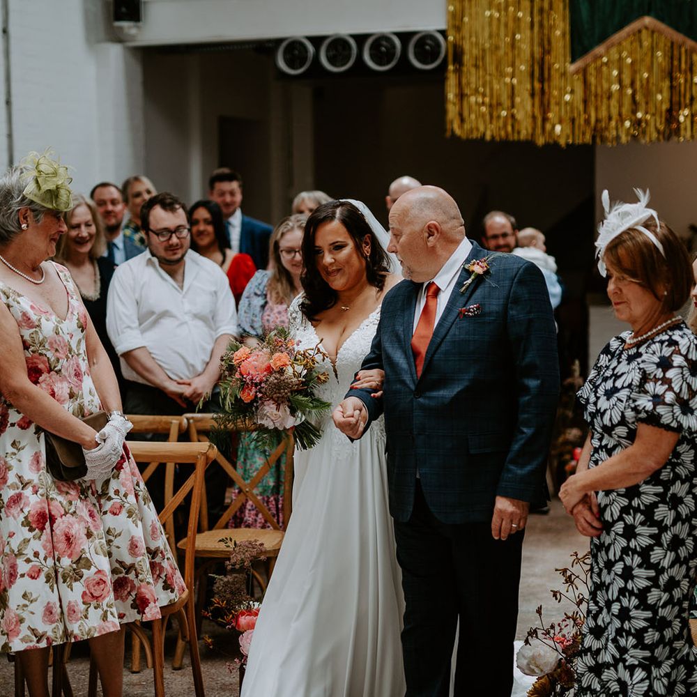 Bride walks down the aisle with her father during industrial styled wedding ceremony