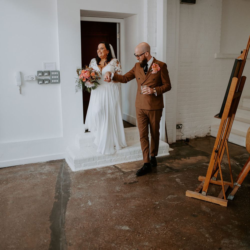 Groom wears 70s styled retro suit and walks alongside his bride in lace fitted wedding dress