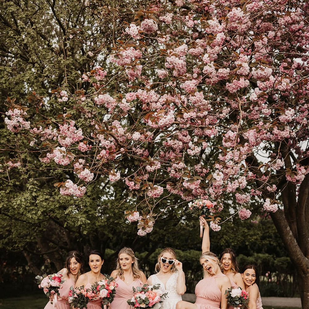 Bridesmaids in pink dresses with the bride in a lace wedding dress and retro sunglasses under a pink blossom tree