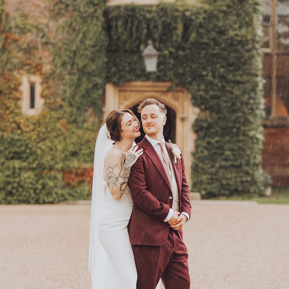 Bride & groom stand in the rain outdoors on their wedding day at St Audries Park