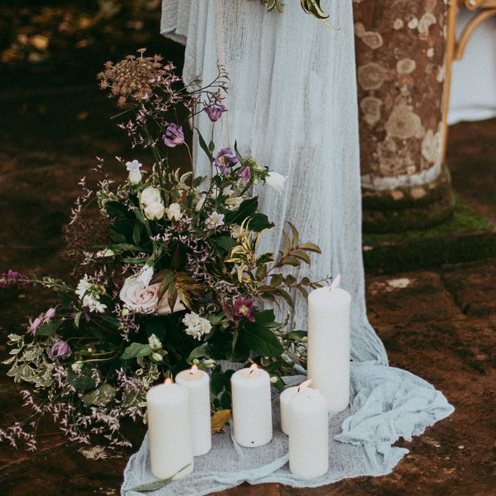 White pillar candles, sheer white drapes and mixed neutral floral decorations with white carnations, purple tulips, roses and foliage
