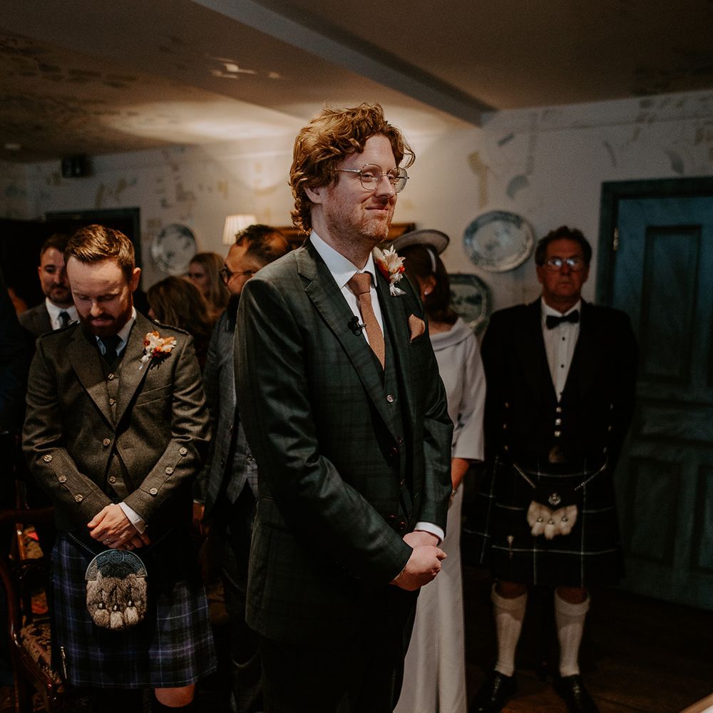 Groom wearing dark suit with orange tie and autumnal boutonniere waiting for bride at the alter of The Zetter Townhouse 