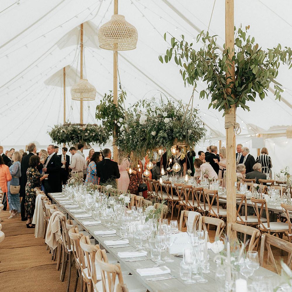 Marquee wedding reception complete with wooden banquet tables, hanging green foliage installations and fairy lights