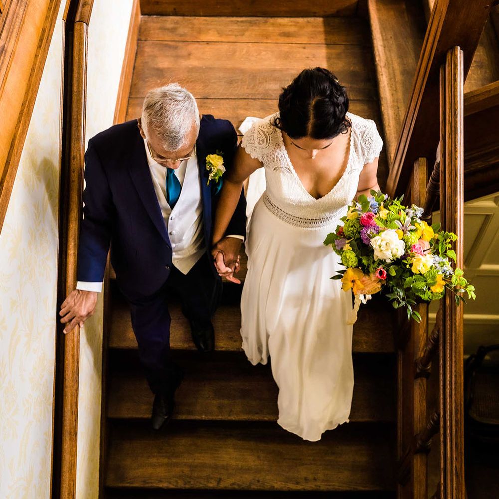 Bride walks down the stairs with her father on the morning of her wedding day before outdoor ceremony 