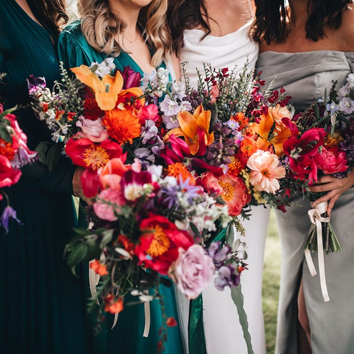 Bright and colourful bride and bridesmaid bouquets with pink, red, orange, and purple flowers including lilies and wax flowers