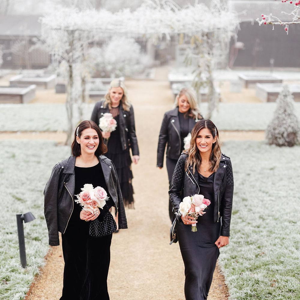Bridesmaids in black bridesmaid dresses with matching leather jackets with small bouquets of pale pink roses 