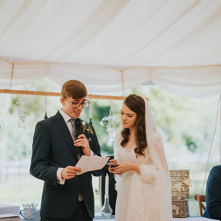 The bride and groom stand at their marquee wedding to read out their joint wedding speech 