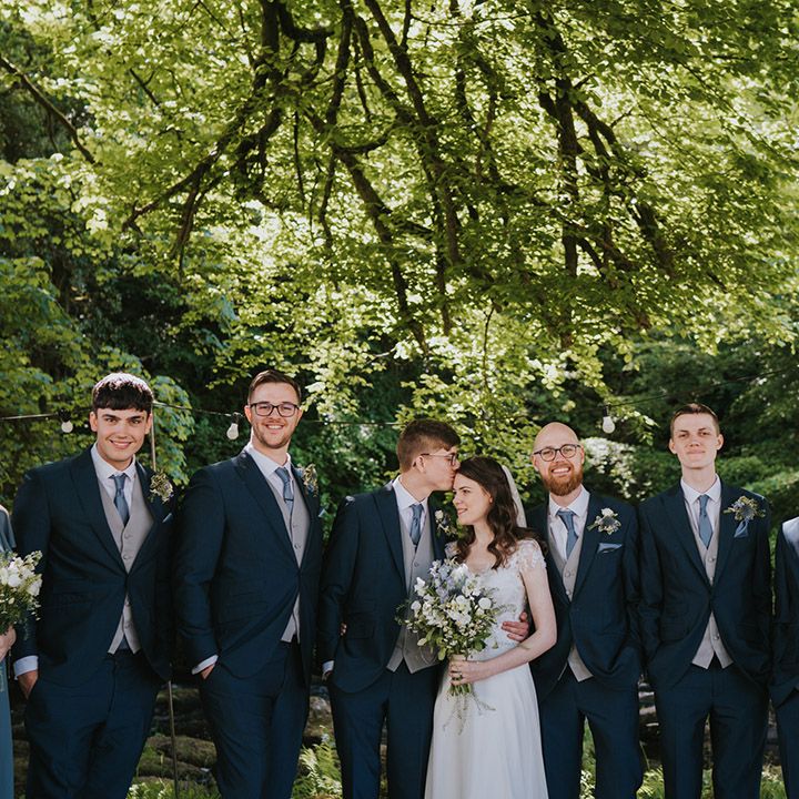 Bridesmaids in blue ruffle bridesmaid dresses with the groom and groomsmen in matching navy suits and the bride in a beaded embellished wedding dress