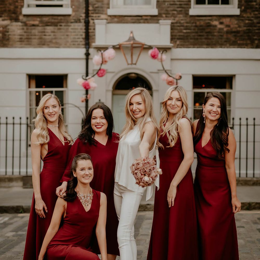 Bride in sleek bridal suit with bridal party in mismatched burgundy bridesmaid dresses at The Zetter Townhouse 