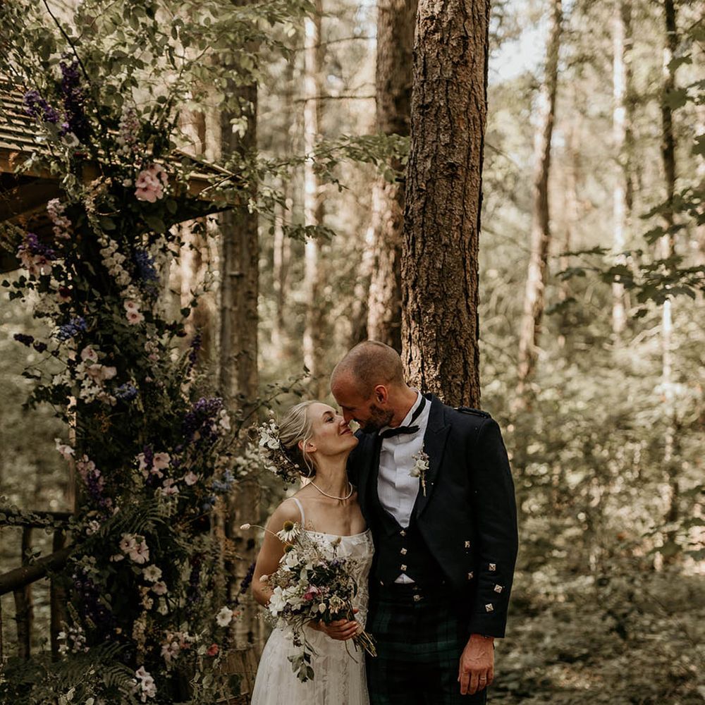 Bride in floral wedding dress and groom in black tie posing together for a cute couple portrait at their woodland Yorkshire wedding venue