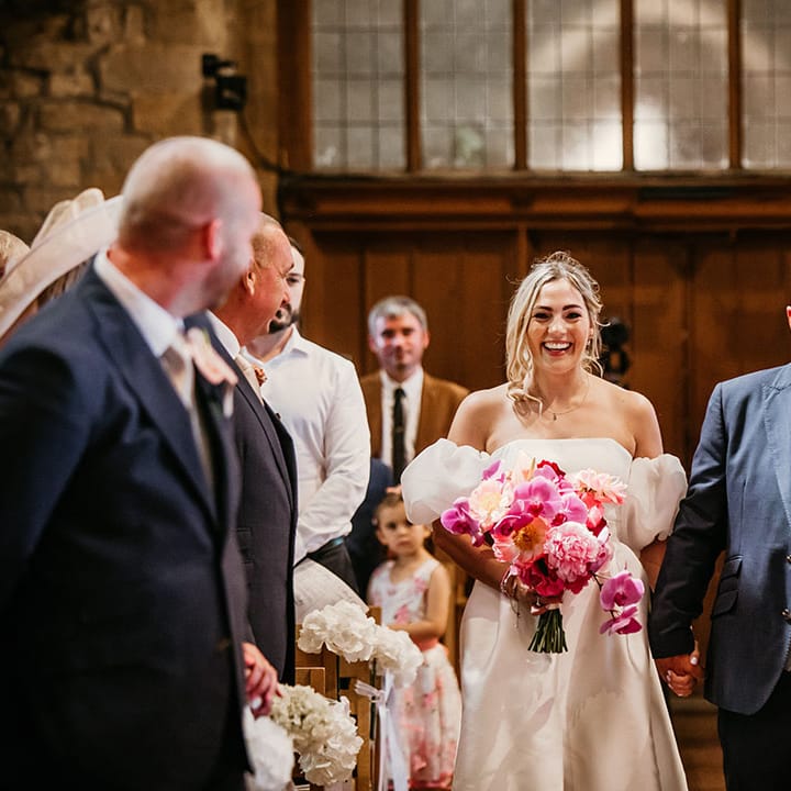 Bride carrying bright pink wedding bouquet walking back down the aisle with the groom in a navy suit 