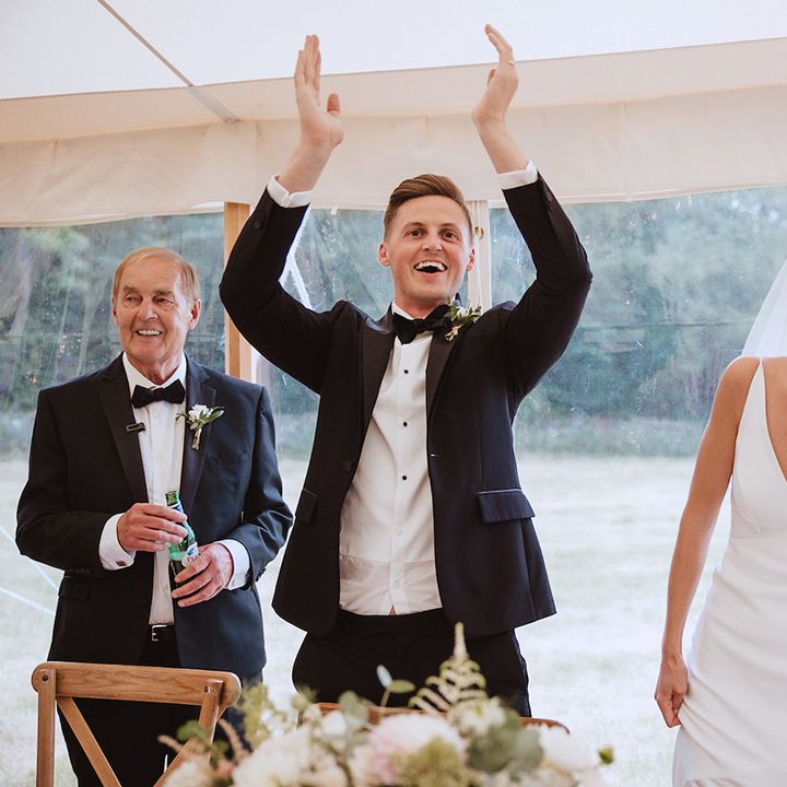 Groom in black tie tuxedo with bride in satin slip gown at marquee reception 