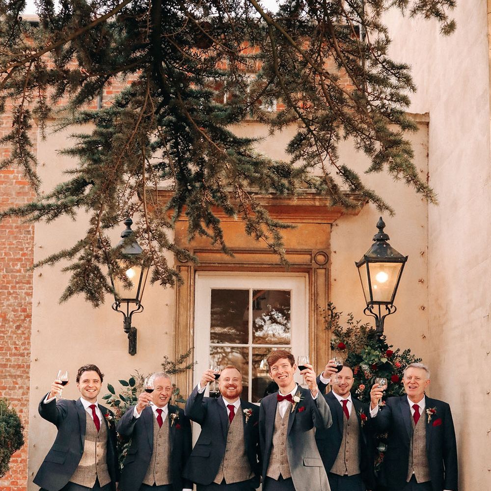Groom and groomsmen holding glasses of red wine a the winter Christmas wedding 