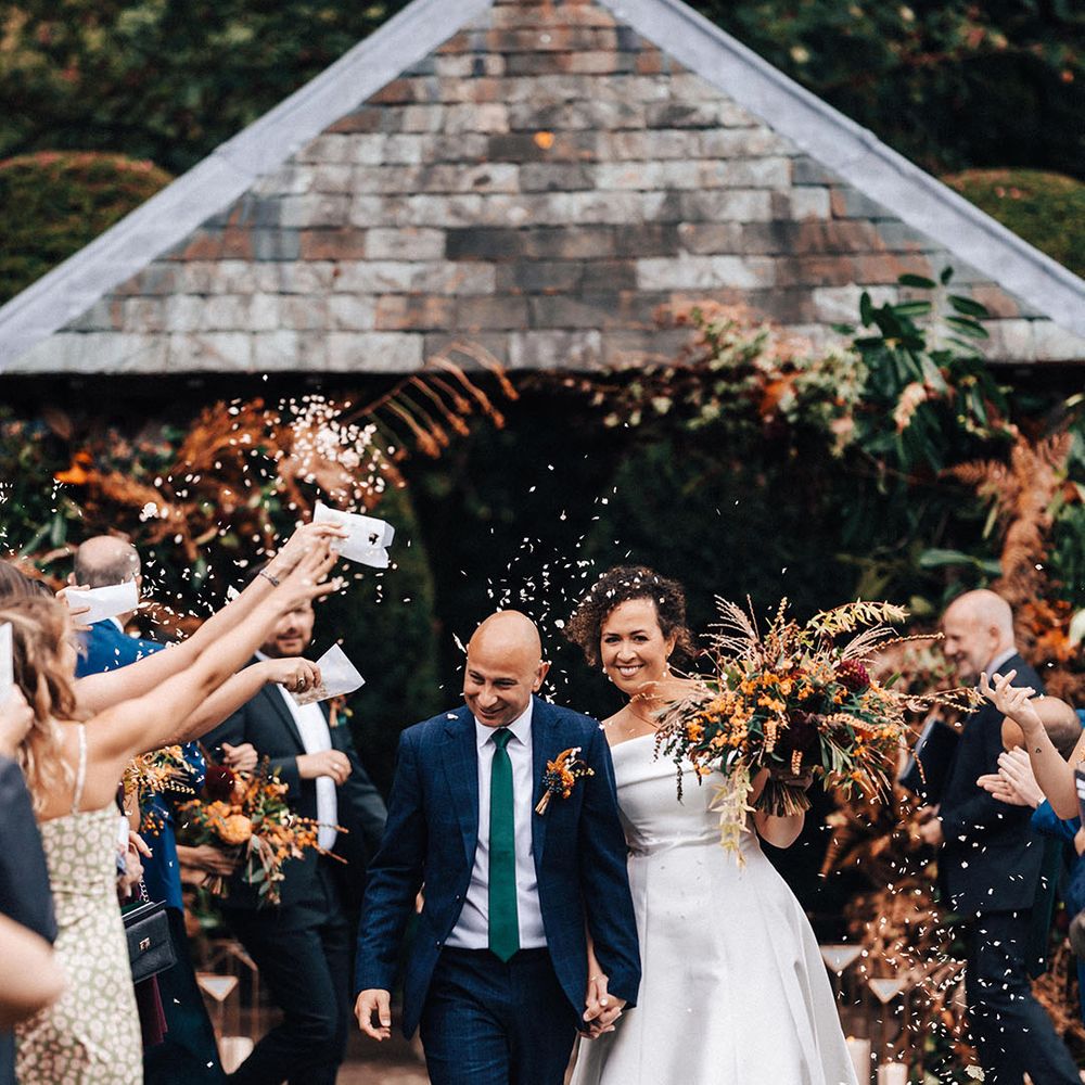 Confetti moment at outdoor wedding with the bride carrying an autumnal orange wedding bouquet 